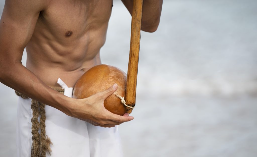 Capoeirista segurando berimbau na praia